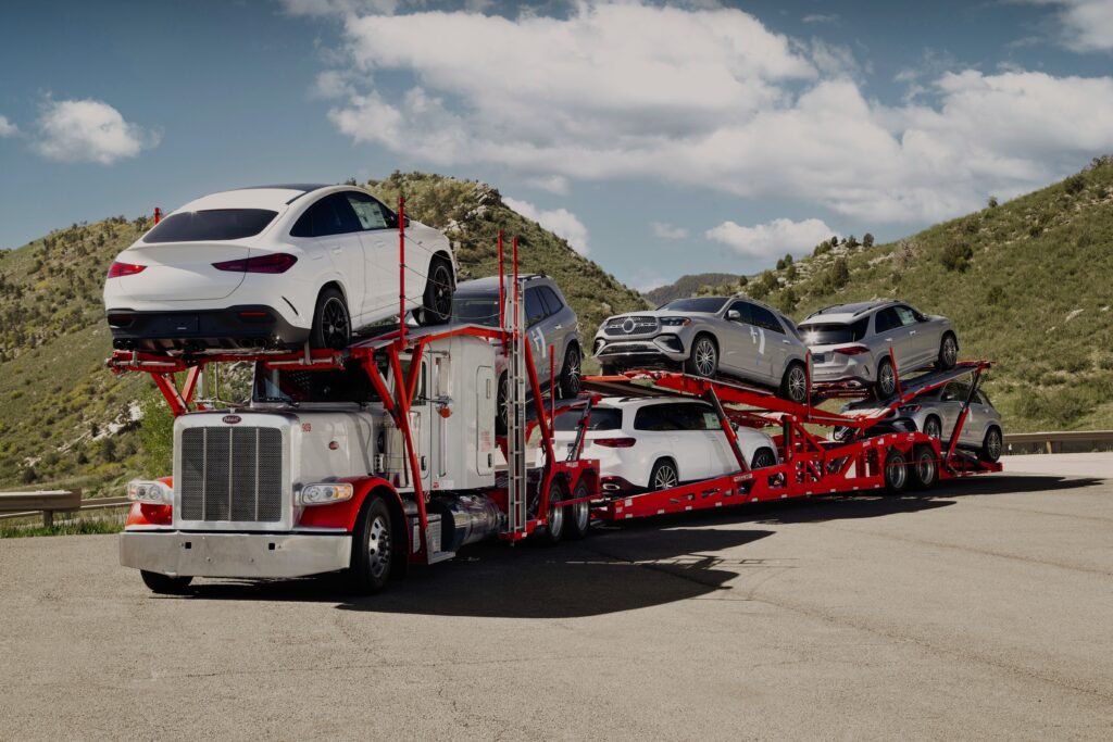 Loaded car hauler parked on a hillside road, with SUVs over the cab and on both trailer decks